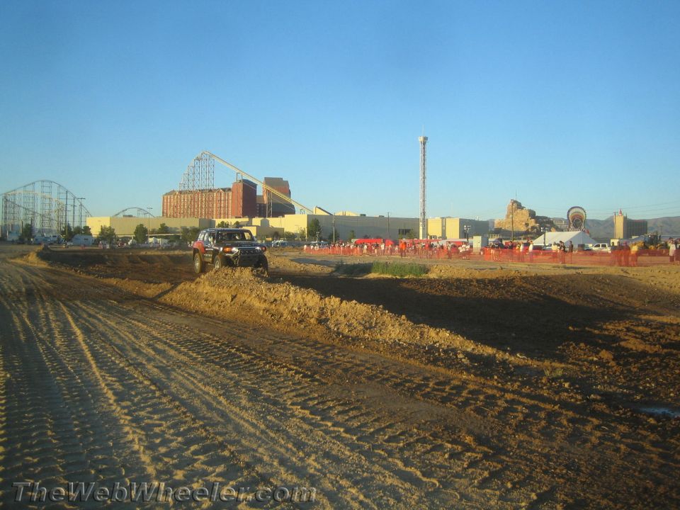 Red and black truck crossing a dirt berm with buildings behind