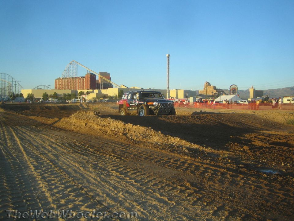 Boxy off-road SUV on a dirt course with a roller coaster behind