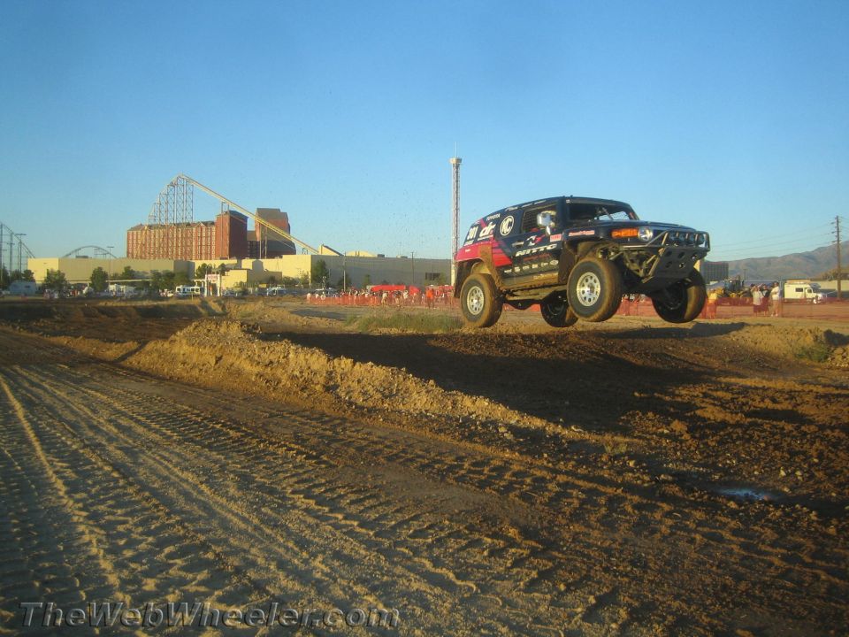 Boxy off-road SUV airborne over a dirt jump under blue sky