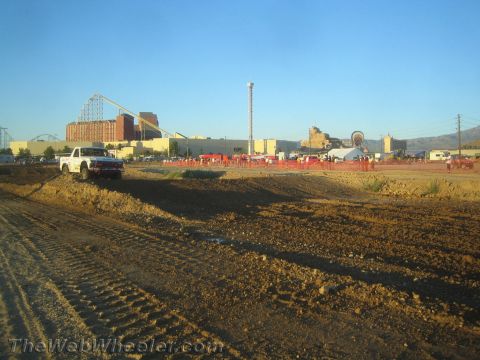 1990 Ford Bronco - white pickup truck sits on a graded dirt course backed by buildings, a tower ride and a roller coaster.