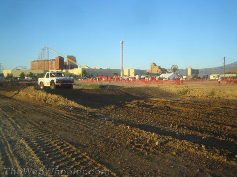 1990 Ford Bronco - white lifted pickup truck crosses a dirt berm on a desert course with a roller coaster behind.