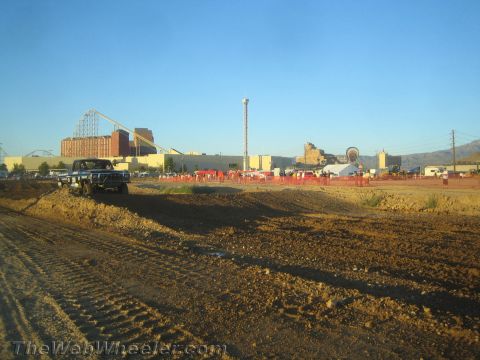 1990 Ford Bronco - graded dirt off-road racing course with a dark pickup truck staged at left and a roller coaster and buildings in the distance.