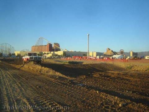 1990 Ford Bronco - wide dirt off-road racing course with a pickup truck at left and a roller coaster and buildings in the distance.