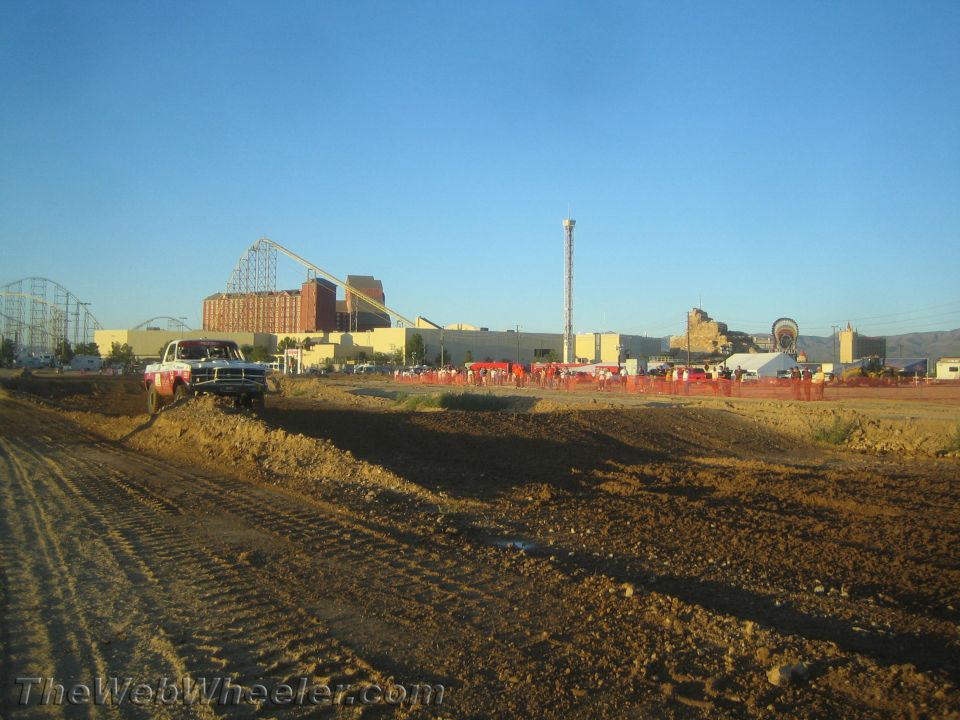 Dirt off-road course with a pickup at left and roller coaster in distance
