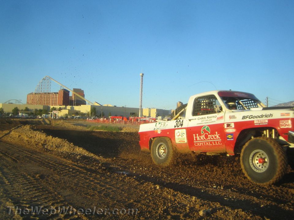 Red and white number 304 race truck cornering hard on dirt at dusk