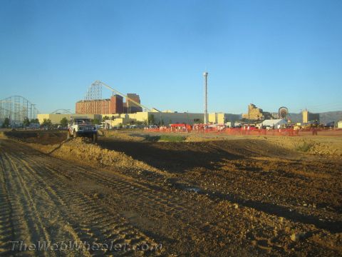1990 Ford Bronco - graded dirt off-road racing course with a light pickup at left and a roller coaster, buildings and crowd in the distance.