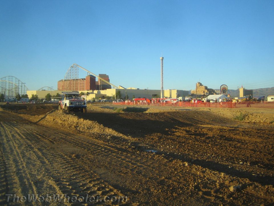 Dark pickup on a dirt off-road course with roller coaster in distance