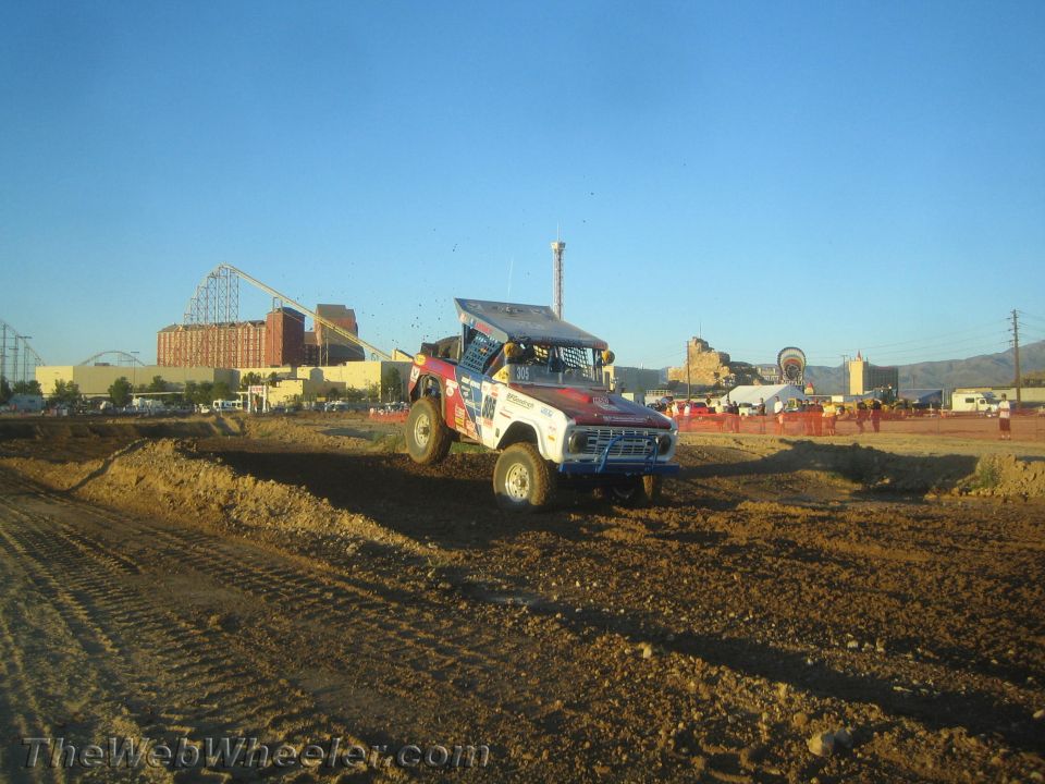Blue and white race truck cresting a dirt rise on the track at dusk