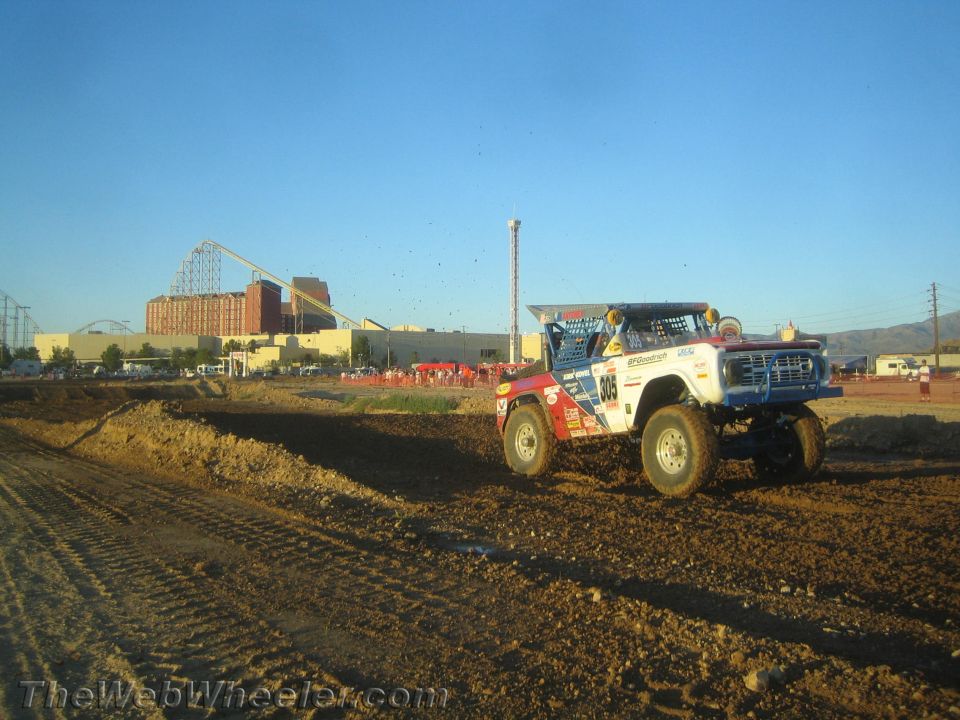 Red, white and blue off-road race truck climbing a dirt berm at dusk