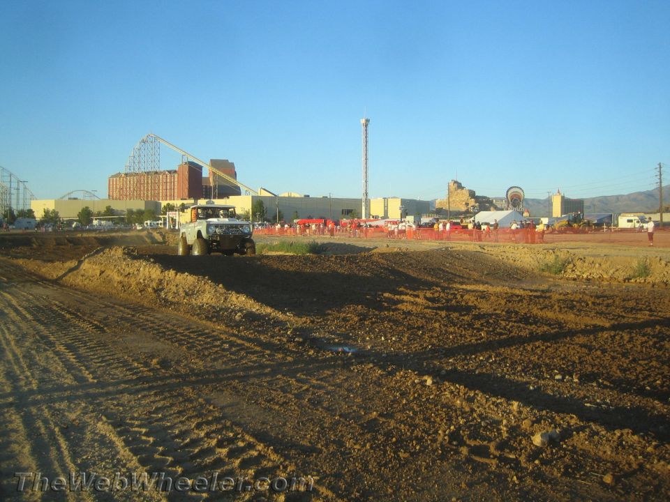 Light off-road truck on a dirt course with roller coaster and crowd behind