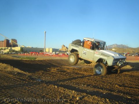 1990 Ford Bronco - light-colored off-road race truck numbered 348 with a roof-mounted spare slides through a dirt corner at golden hour.