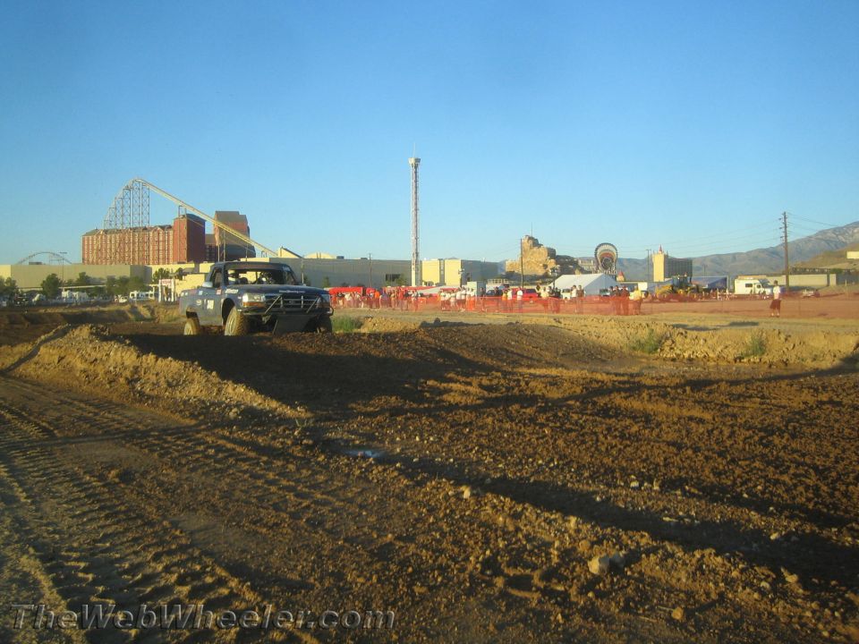 Lifted pickup truck on a dirt off-road course with amusement park rides in the background