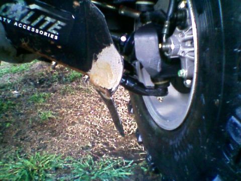1992 Ford F-150 - Low ground-level view of a front wheel and suspension showing a black skid plate or CV guard torn open with bare metal exposed at the gouge…