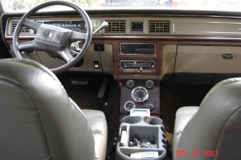 1989 Ford Crown Victoria LTD - The interior of a car shows tan seats, wood trim, and a dashboard with a radio and aftermarket gauges.