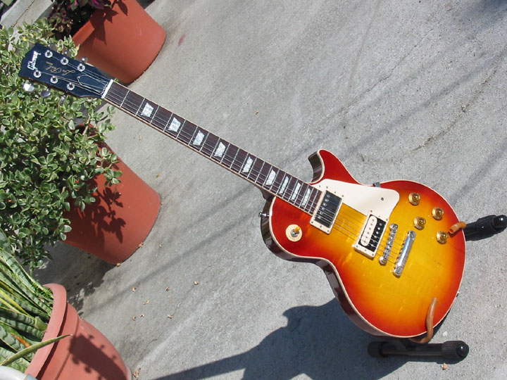 Sunburst electric guitar with white pickguard and chrome hardware, resting on a stand