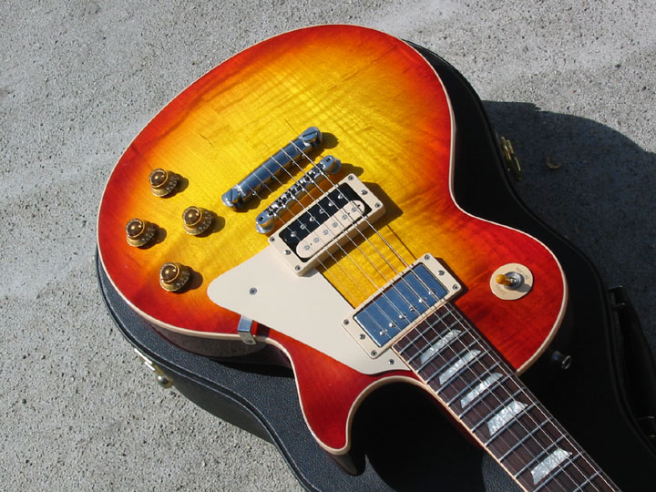 Sunburst electric guitar with cream pickguard and chrome hardware, in its case on concrete