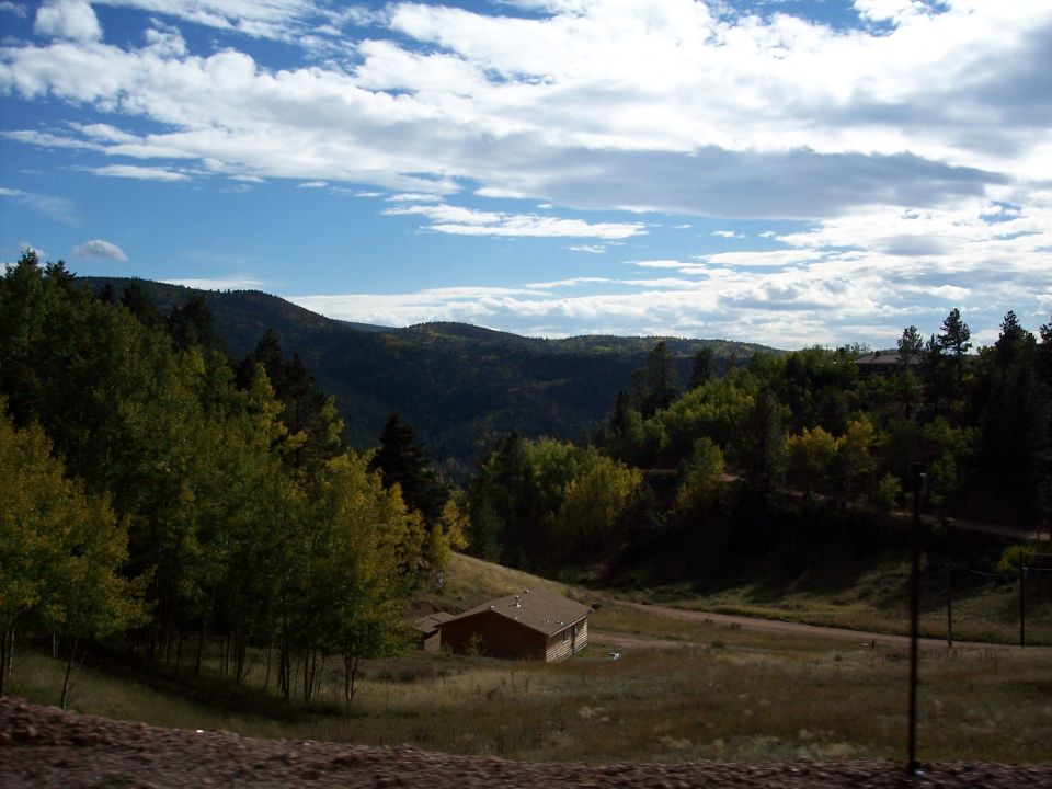 Mountainous landscape with trees and a small building under a cloudy sky