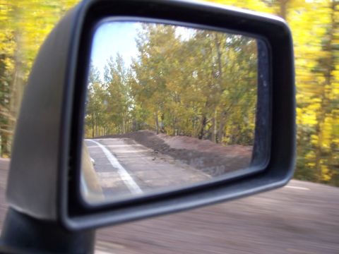 1972 Ford Ranchero - A view through a car's side mirror shows a road winding through trees with yellow and green foliage.