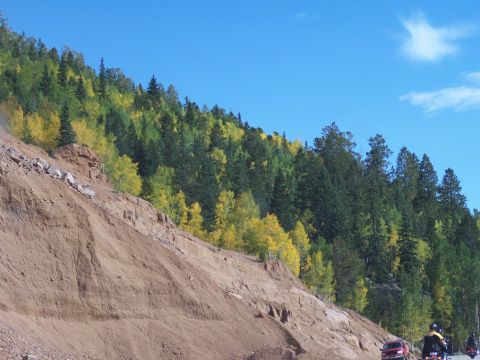 1972 Ford Ranchero - Vehicles travel along a road beside a steep, eroded hillside covered in trees displaying fall colors.