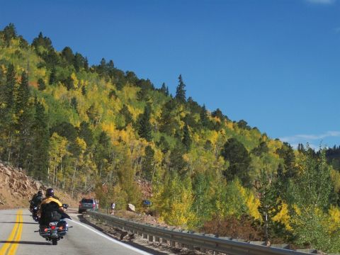 1972 Ford Ranchero - Motorcycles and a car travel along a scenic road bordered by a guardrail and a hillside ablaze with autumn colors.