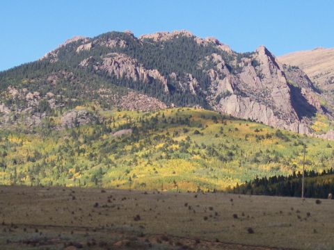 1972 Ford Ranchero - A vast mountain landscape displays a mix of evergreen and deciduous trees, with rocky outcrops dominating the upper slopes.