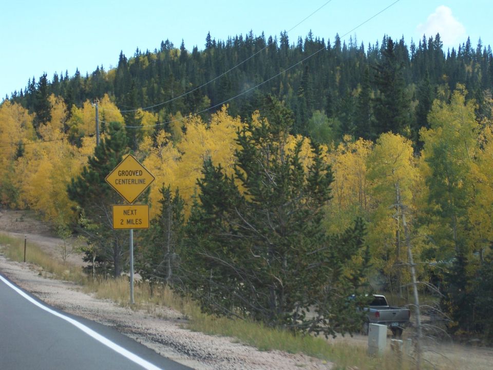 Silver pickup truck parked near a mailbox with fall foliage and pine trees