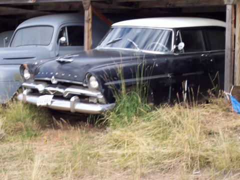 1972 Ford Ranchero - A vintage Plymouth sedan, possibly from the mid-1950s, sits under a wooden shelter next to another vehicle.