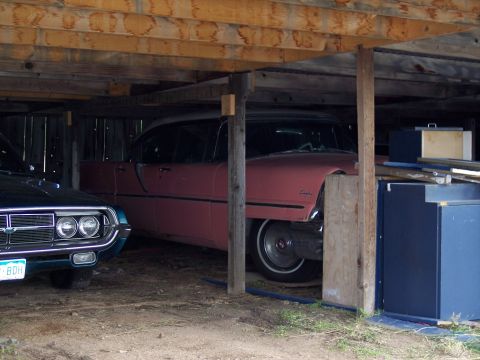 1972 Ford Ranchero - A pink sedan is parked under a wooden structure, partially obscured by supports and other items.