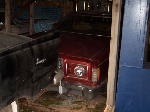 1972 Ford Ranchero - A red car is parked inside a structure, with its front end visible and partially blocked by a black vehicle.