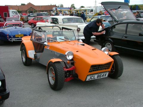 2001 Ford Fiesta - Outdoor car show with multiple vehicles, including an orange and silver sports car.