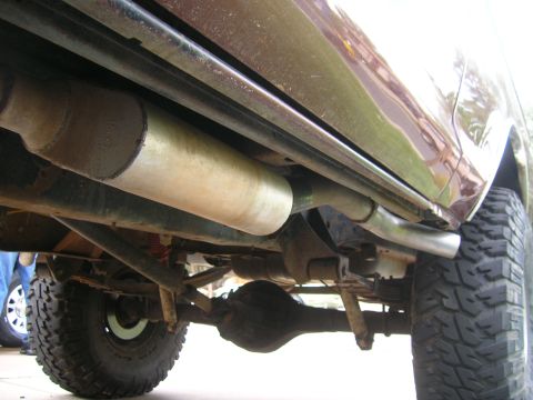 1979 Ford Bronco - Close-up view of the exhaust system and undercarriage components of a vehicle, showing the muffler and suspension.