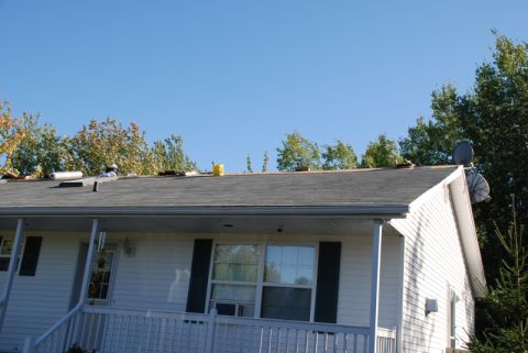 1996 Ford Bronco - A residential roof is partially covered with shingles and construction supplies, with trees in the background.