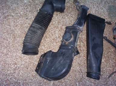 1988 Ford Bronco - Three black plastic and rubber air intake pieces arranged on tan carpet: a ribbed flexible accordion hose, a molded fender-mounted cold-air…