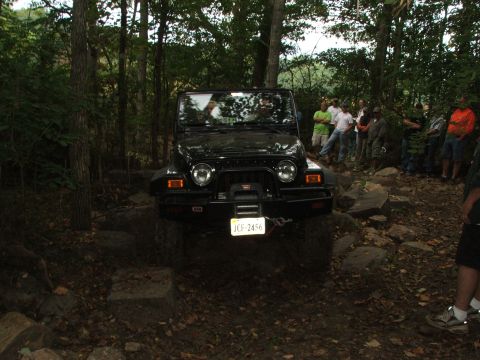 1996 Ford Bronco - A black Jeep Wrangler TJ is shown off-road on a rocky trail with spectators watching.