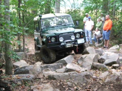 1996 Ford Bronco - A group of people watch as a green Land Rover Defender 90 navigates a rocky off-road course.