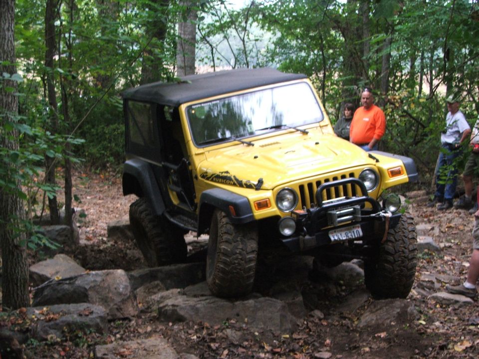 Yellow Jeep Wrangler Rubicon with a black soft top navigating a rocky trail, front winch visible