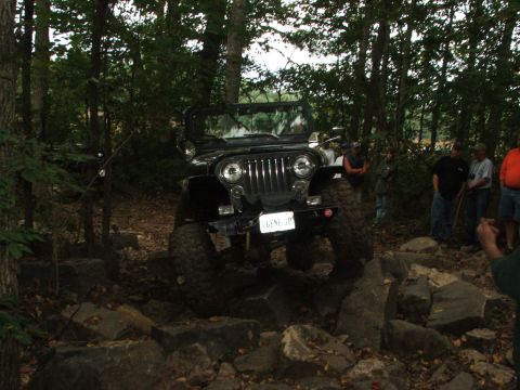 1996 Ford Bronco - A black Jeep Wrangler tackles a challenging off-road course with onlookers present.