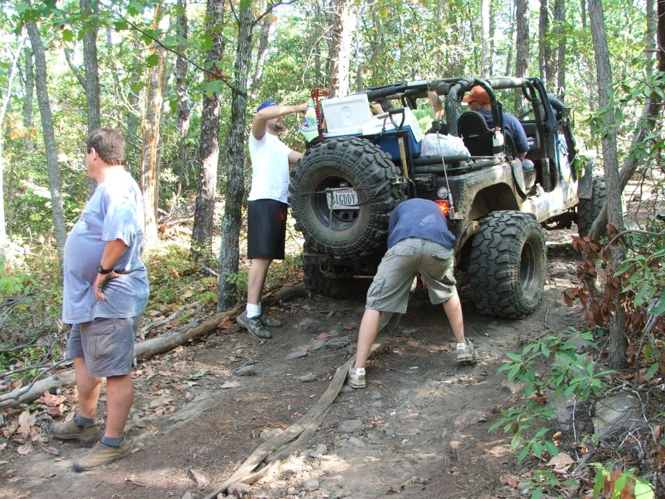 Off-road Jeep with large tires, spare tire mounted on rear, people working on it
