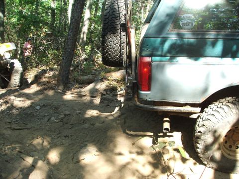 1996 Ford Bronco - A Ford Bronco navigates a wooded off-road trail with a spare tire mounted on the back.
