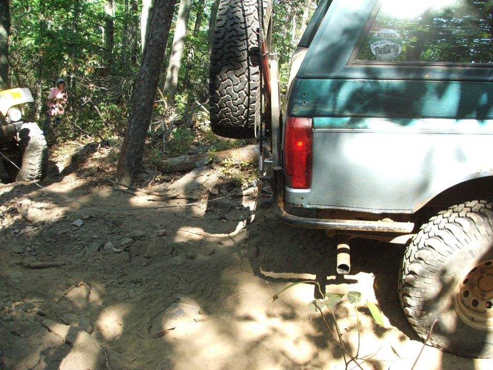 Green and silver Ford Bronco with spare tire mounted on rear, off-road tires, and exhaust pipe