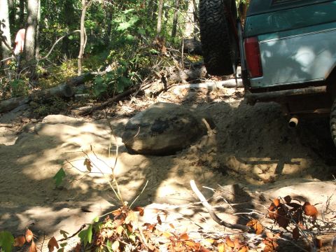 1996 Ford Bronco - An SUV with a spare tire on the back navigates a challenging sandy and rocky off-road trail.