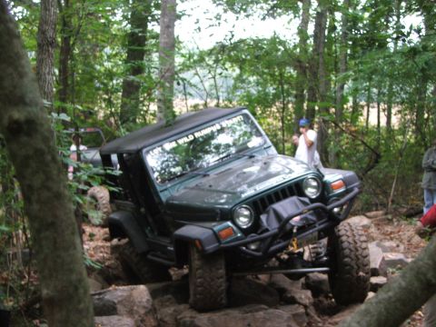 1996 Ford Bronco - A green Jeep Wrangler navigates a rocky trail with people watching in the background.
