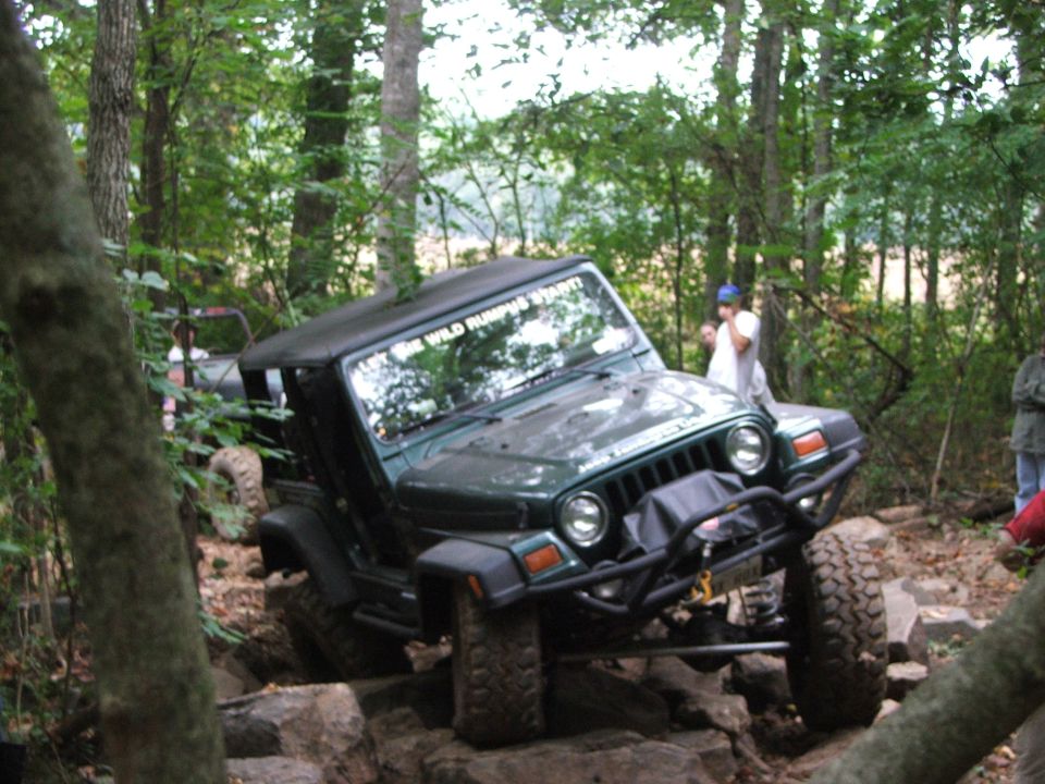 Green Jeep Wrangler on rocks, front bumper, soft top, windshield sticker