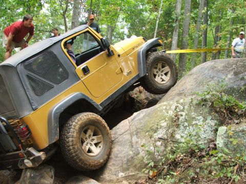 1996 Ford Bronco - Yellow Jeep Wrangler Rubicon navigating a difficult rocky obstacle on an off-road trail.