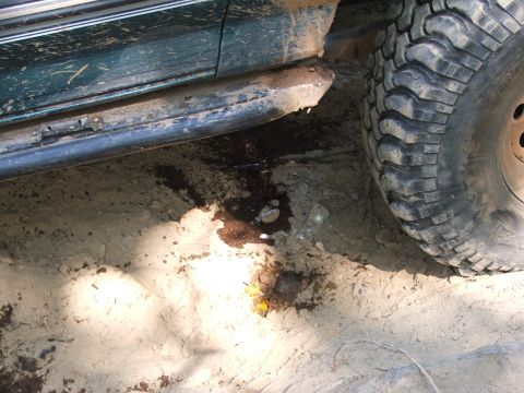 1996 Ford Bronco - Side view of a mud-splattered green SUV with a large tire and a fluid leak on the ground.