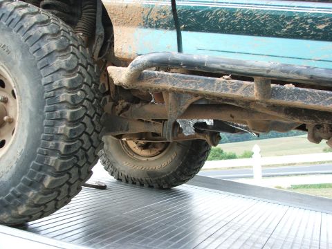 1996 Ford Bronco - Close-up of the undercarriage and large tires of a mud-splattered green SUV loaded onto a flatbed trailer.