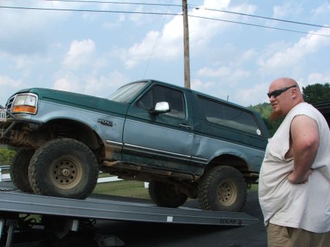 1996 Ford Bronco - A man stands next to a lifted Ford Bronco being loaded onto a tow truck.