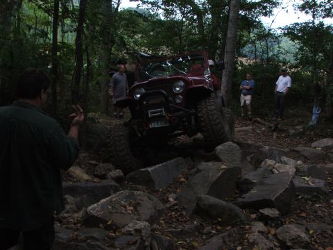 1996 Ford Bronco - A red Jeep Wrangler navigates a challenging rocky trail with onlookers present.