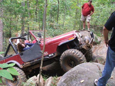 1996 Ford Bronco - A red Jeep navigates a difficult rocky terrain with onlookers observing the off-road challenge.