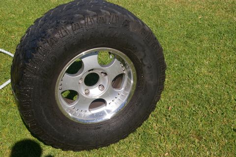 1986 Ford Bronco - A single off-road tire and rim rests on a grassy lawn, possibly after being cleaned.